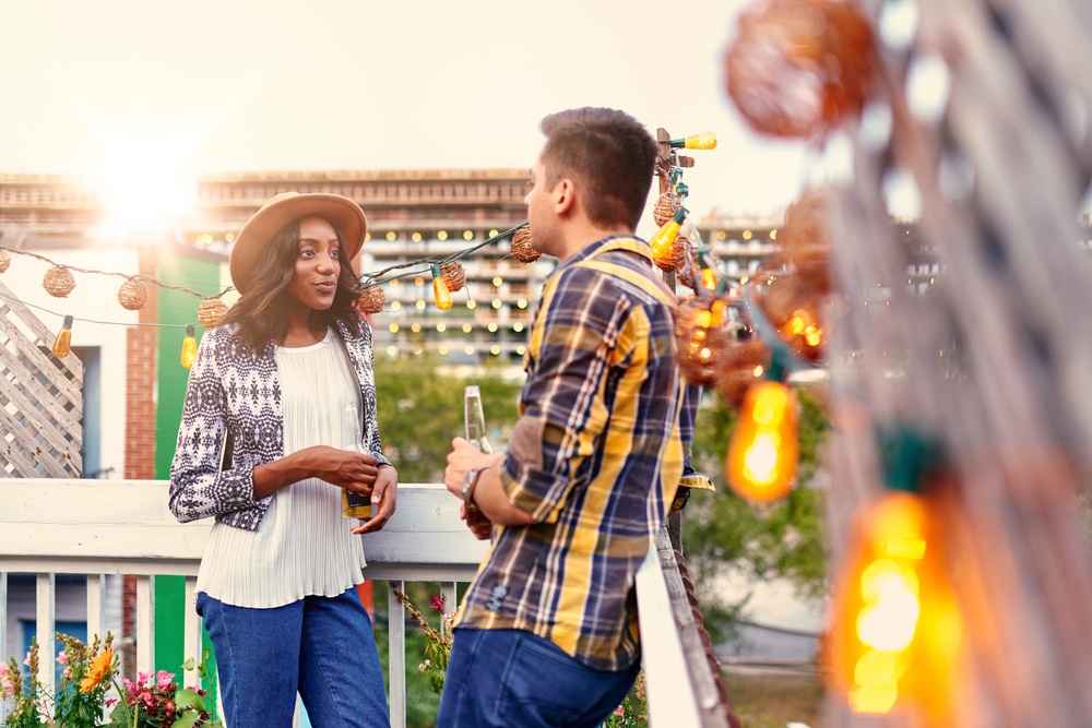 Multi-ethnic millenial couple flirting while having a drink on rooftop terrasse at sunset.jpeg