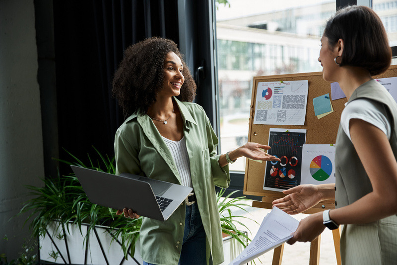 Women discuss business growth on a cork board with marketing metrics